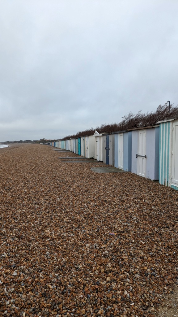 A line of beach huts at Bognor Regis with the stony beach and sea in front on the keft